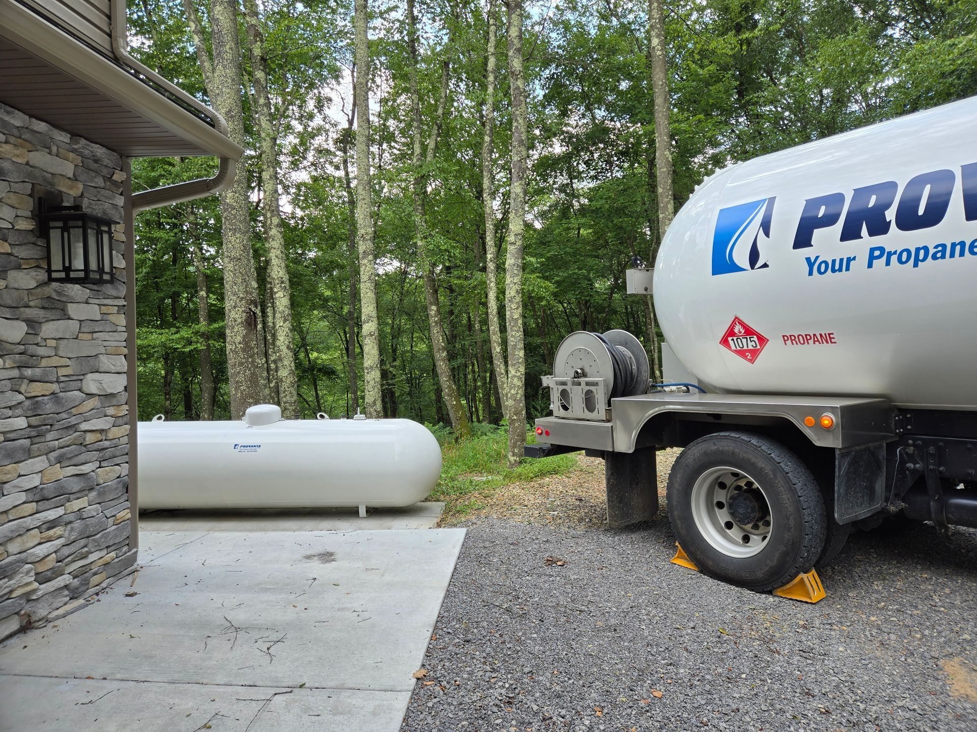 A crane lifts a large white tank. A worker guides the tank near another tank. Outdoors on green grass.