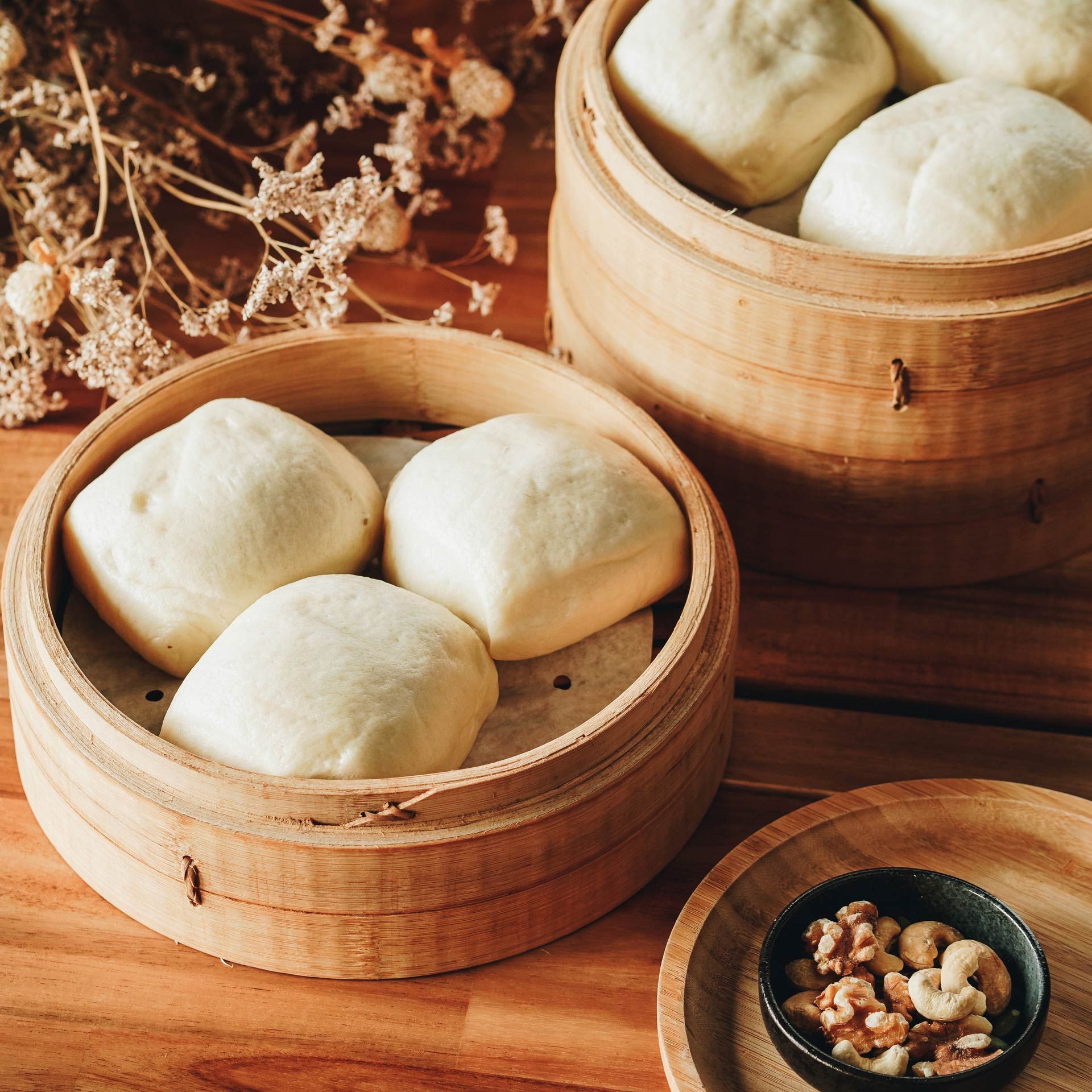 Three bamboo steamers filled with dumplings and nuts on a wooden table.