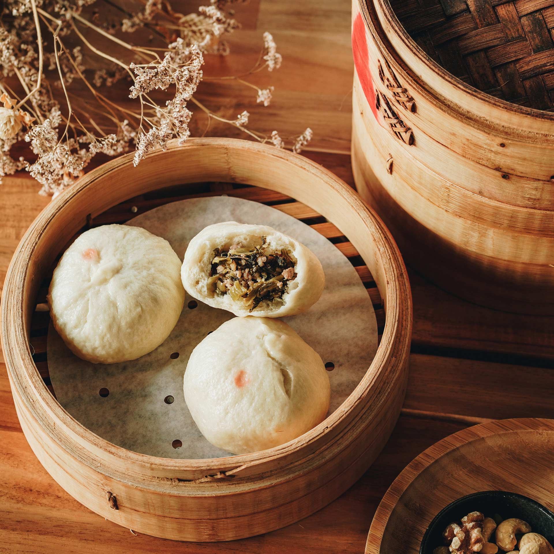 Three dumplings in a bamboo steamer on a wooden table