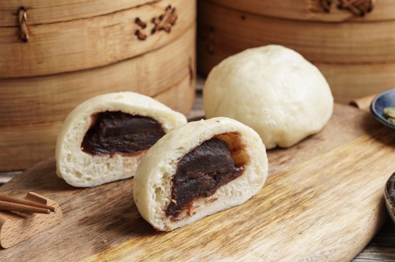 Two buns with red bean filling are sitting on a wooden cutting board.