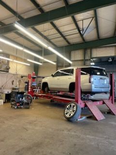 White SUV on a red lift in a garage, one tire removed.