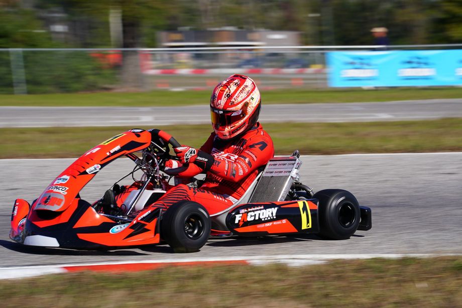 Red go-kart racer cornering on a track at speed, wearing a red helmet and suit.