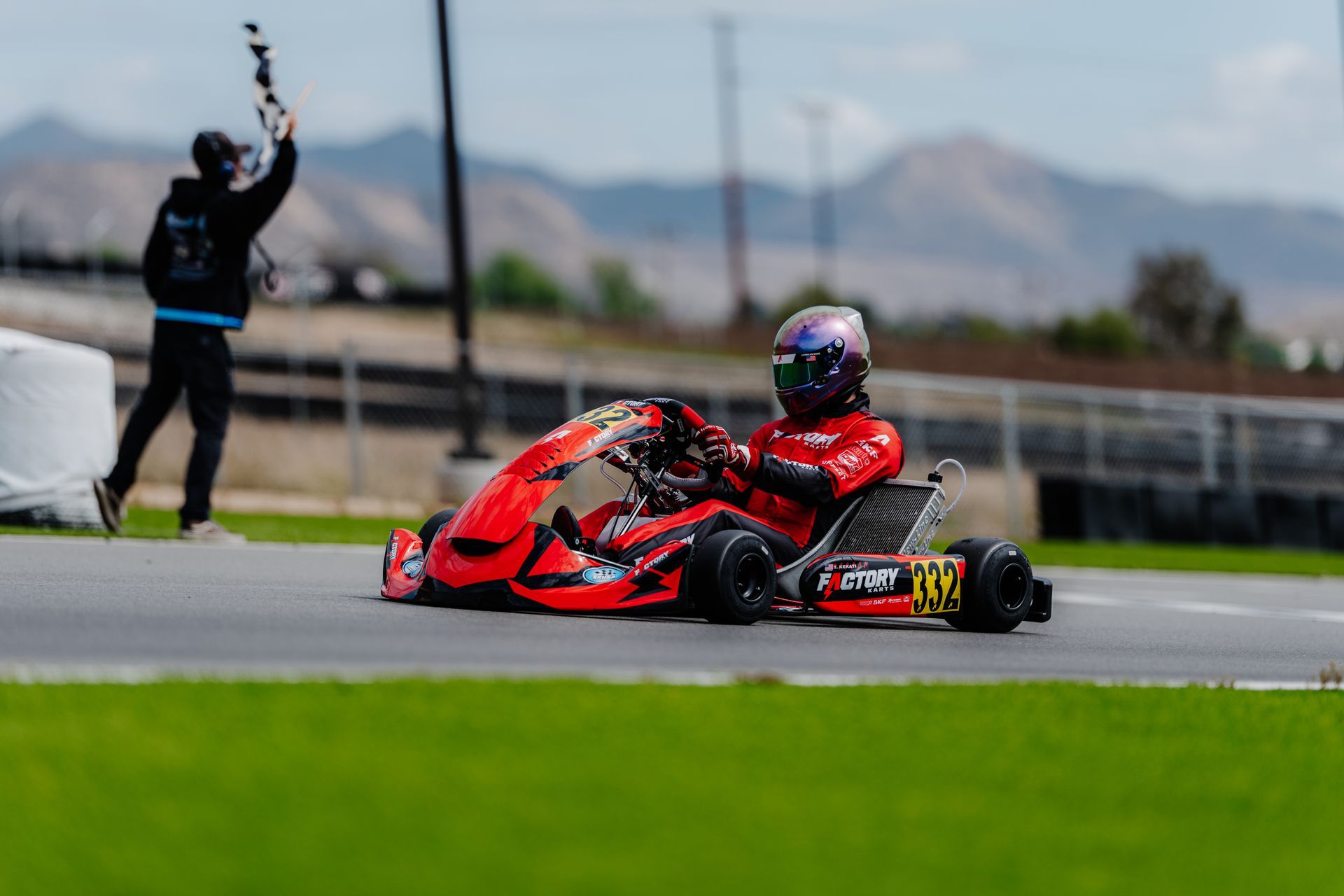 Red go-kart racing on a track, driver leaning into a turn with another kart blurred in the background