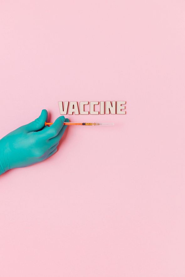A hand in a blue glove is holding a syringe with the word vaccine written on it.