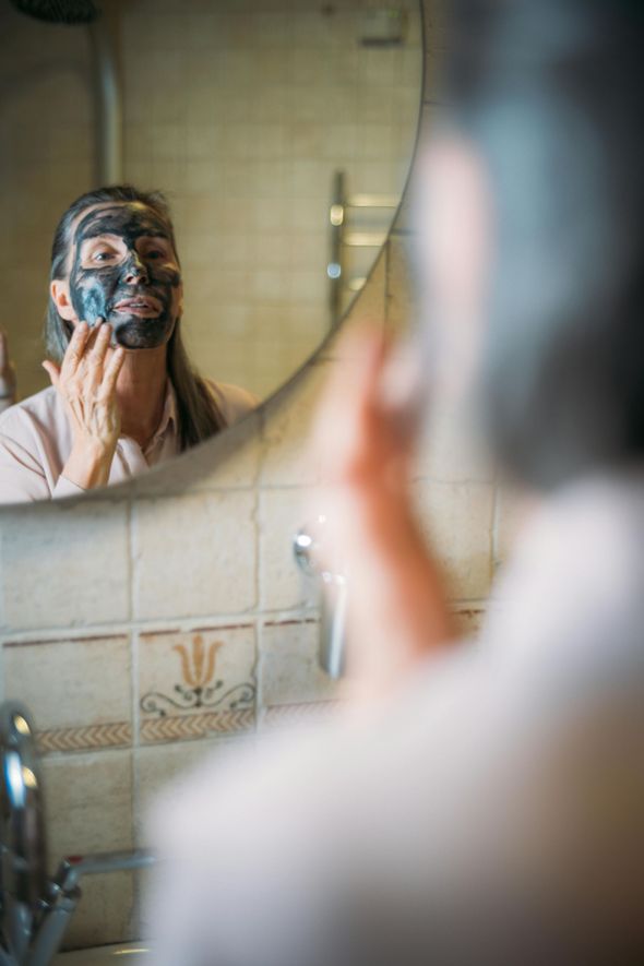 A woman is applying a black mask to her face in front of a mirror.