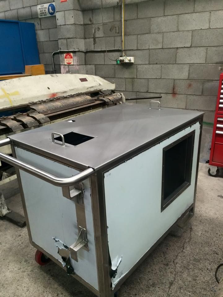 A stainless steel cart is sitting in a warehouse next to a brick wall.