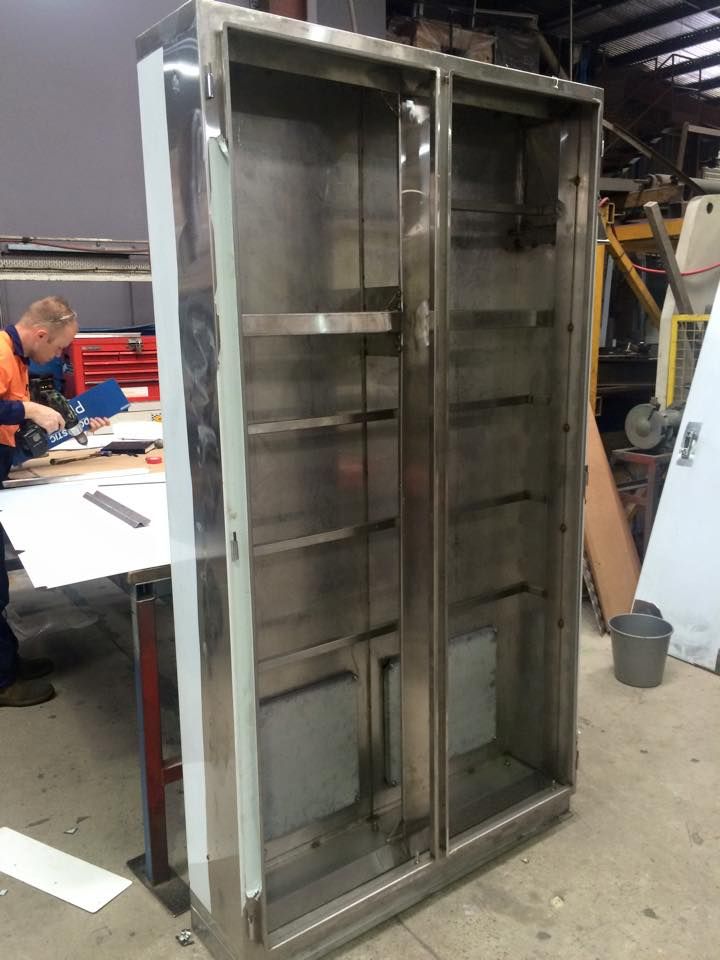 A man is working on a stainless steel cabinet in a factory.
