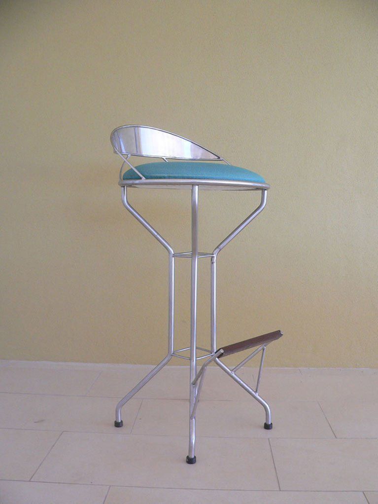 A bar stool with a blue cushion is against a yellow wall