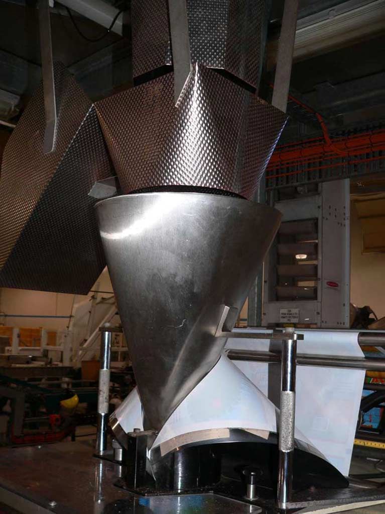 A large stainless steel cone is sitting on top of a table in a factory.
