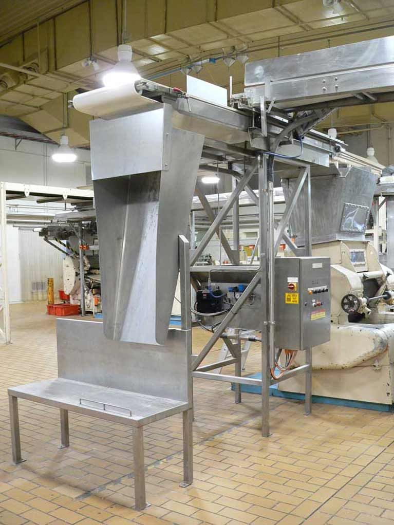 A stainless steel machine is sitting on top of a brick floor in a factory.