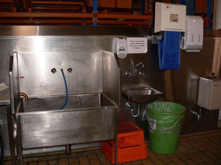A stainless steel sink is in a kitchen next to a green trash can.