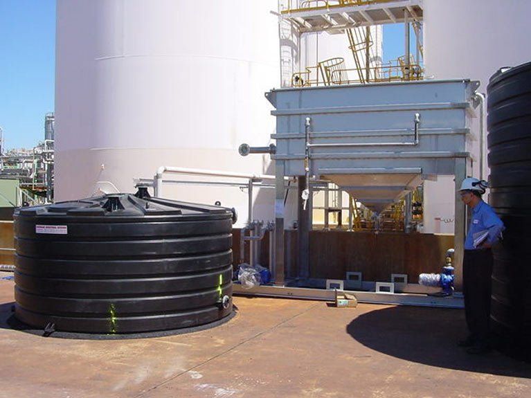 A man in a hard hat is standing in front of a large tank.