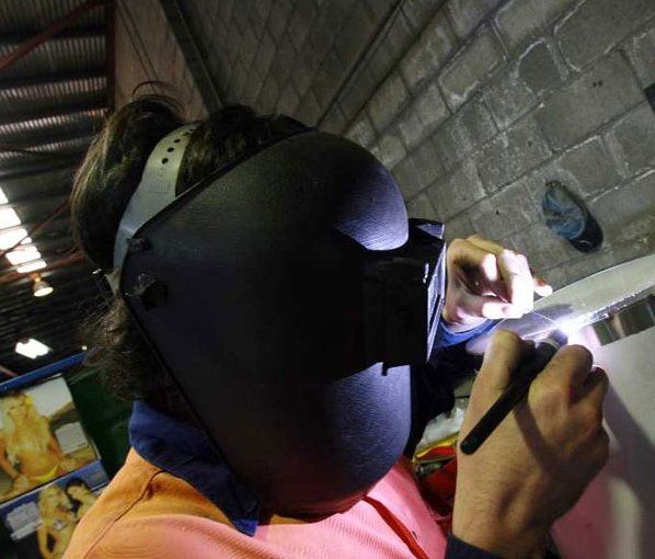 A man wearing a welding mask is working on a piece of metal
