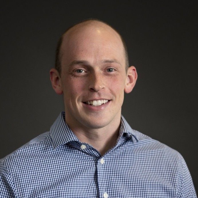 A man wearing a blue and white checkered shirt is smiling for the camera.