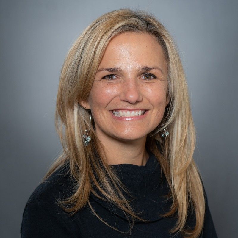 A woman with long blonde hair and earrings is smiling for the camera.