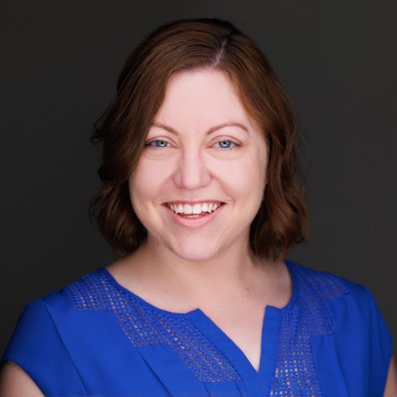 A woman is standing with her arms crossed in front of a red background.