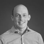 A man in a plaid shirt is smiling in a black and white photo.