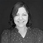 A woman in a polka dot shirt is smiling in a black and white photo.