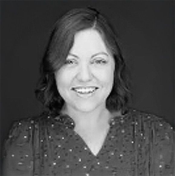 A woman in a polka dot shirt is smiling in a black and white photo.