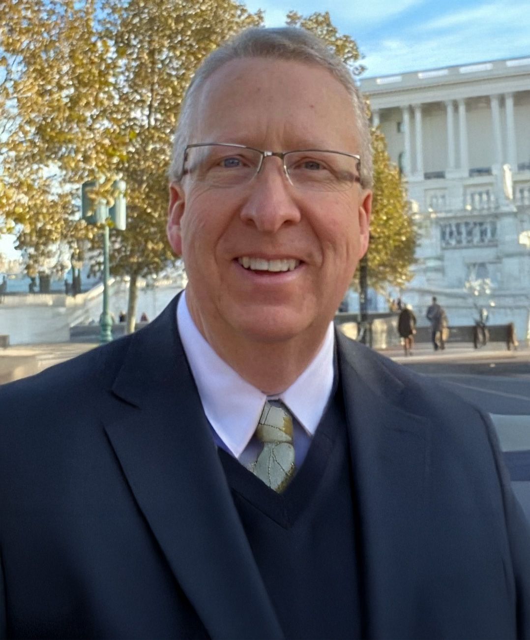 A man in a suit and tie is smiling in front of the capitol building