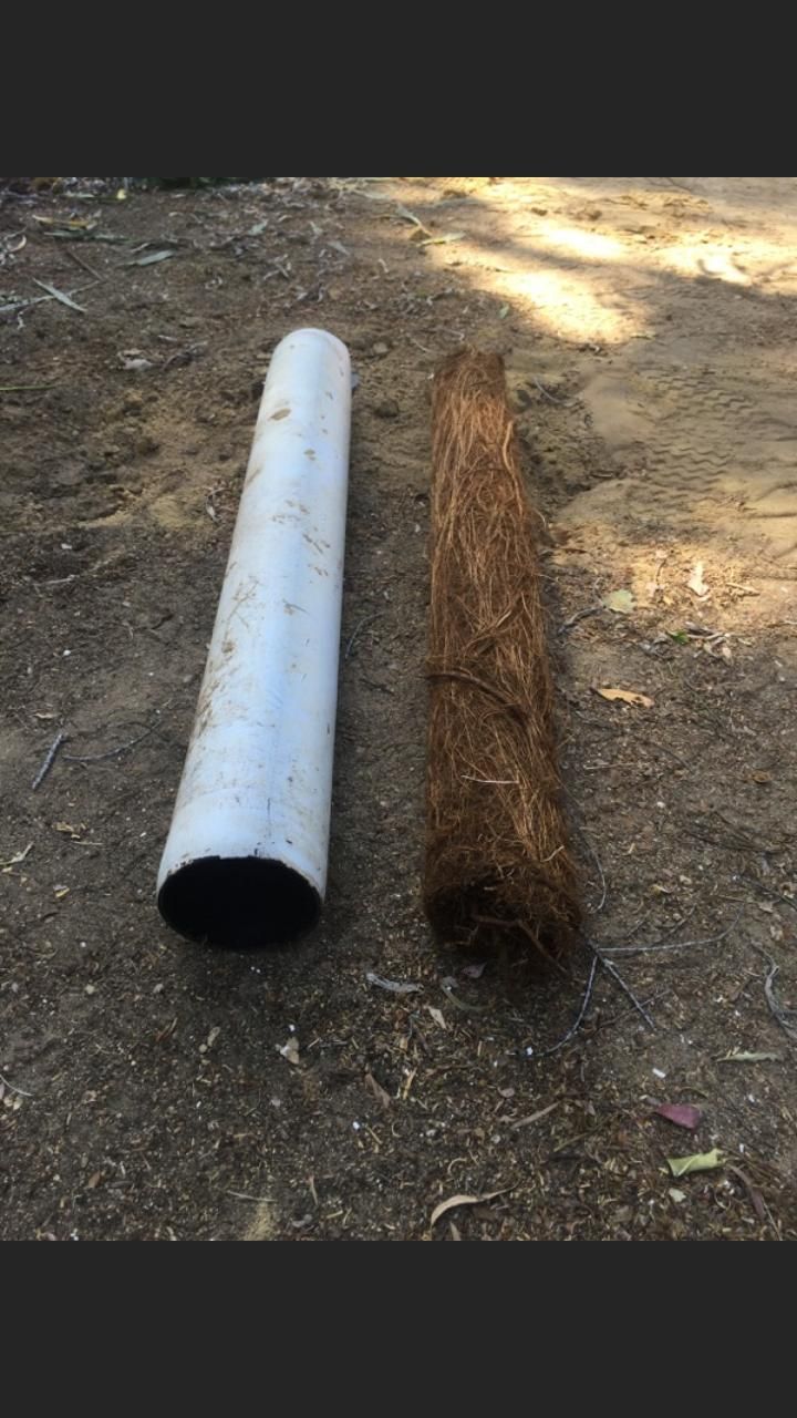 A white pipe and a brown pipe are sitting next to each other on the ground.