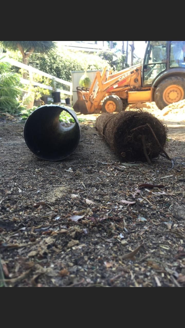 A black pipe is laying on the ground next to a roll of turf.