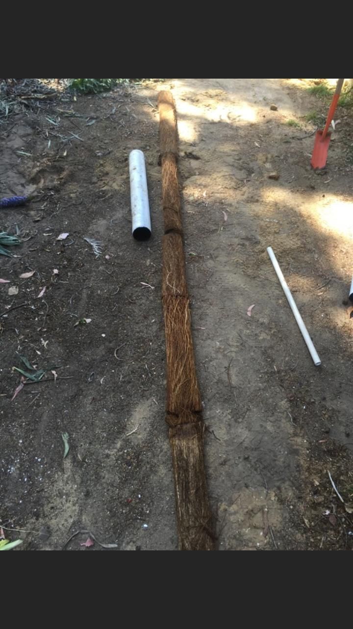 A large piece of wood is sitting on the ground next to a plastic pipe.