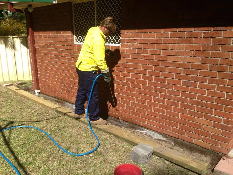 A Man Is Working On A Brick Wall With A Hose — Thermal Imaging Pest Professionals In Raymond Terrace, NSW