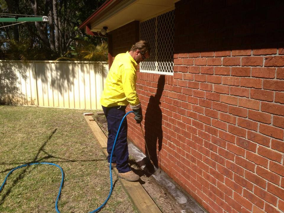 A Person Is Spraying A Brick Wall With A Sprayer — Thermal Imaging Pest Professionals In Raymond Terrace, NSW