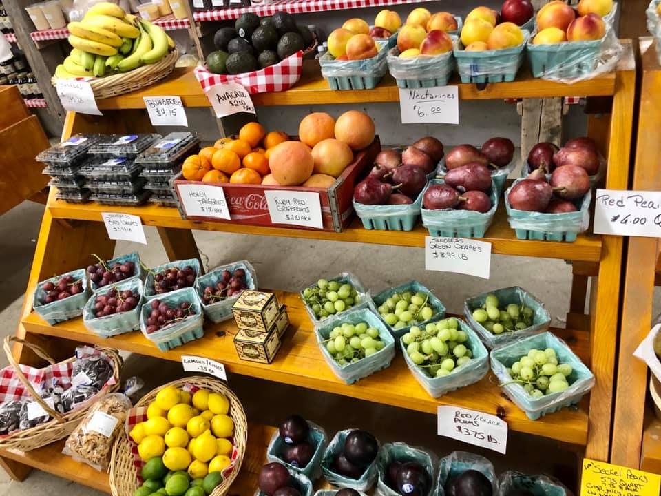 A variety of fruits and vegetables are displayed on a wooden shelf.