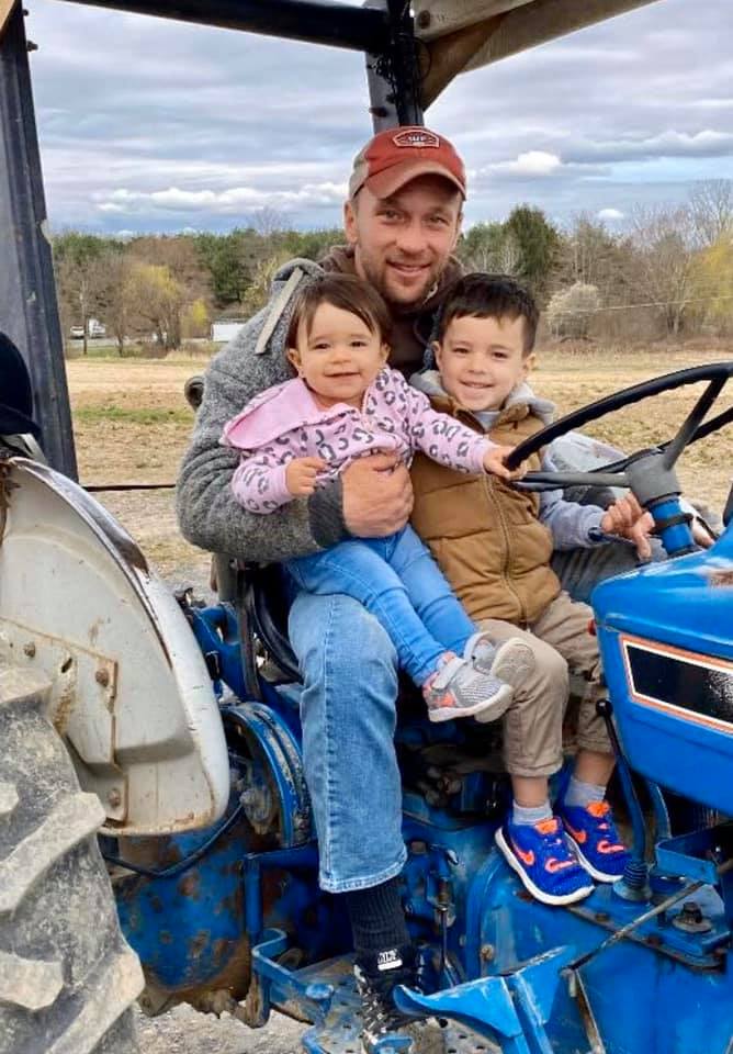 A man is sitting on a blue tractor with two children.