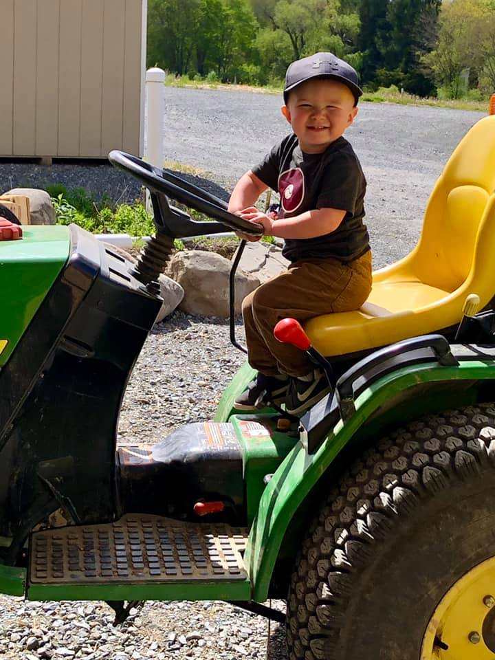 A little boy is sitting on a john deere lawn mower.