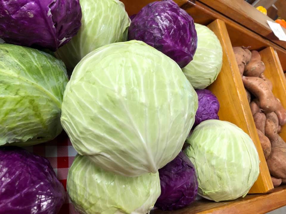 A bunch of cabbage and potatoes are sitting on a wooden shelf.