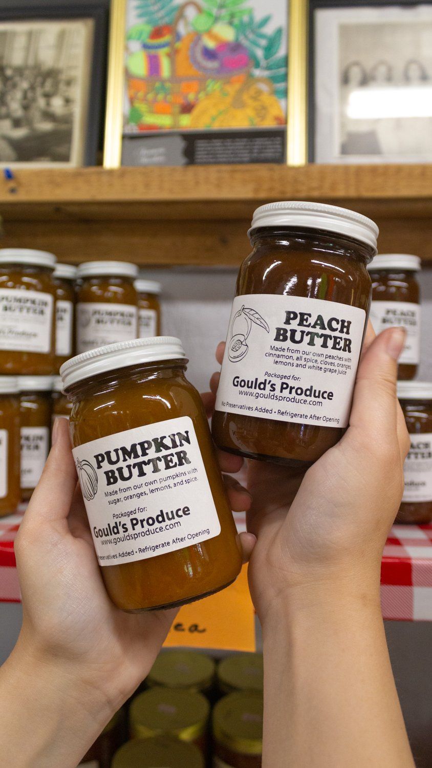 A person is holding two jars of pumpkin butter and peach butter.