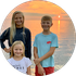 A woman and two children are standing next to each other on the beach at sunset.