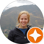 A woman in a black jacket is smiling in front of a mountain.