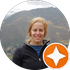A woman in a black jacket is smiling in front of a mountain.