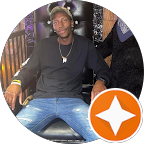 A man in a black shirt and blue jeans is sitting on a chair.