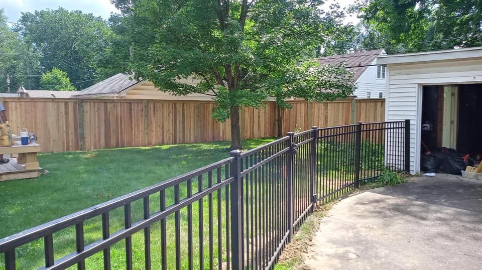 A black metal fence surrounds a backyard with a wooden fence.