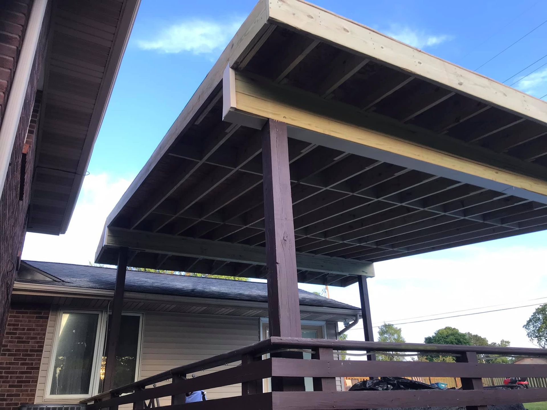 A wooden deck with a canopy over it is in front of a house.