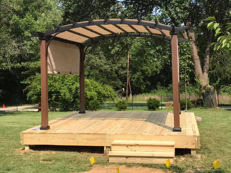 A wooden stage with a pergola on top of it in a park.
