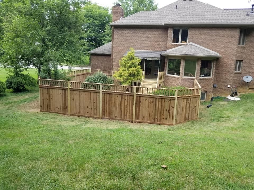 A wooden fence is in the backyard of a brick house.