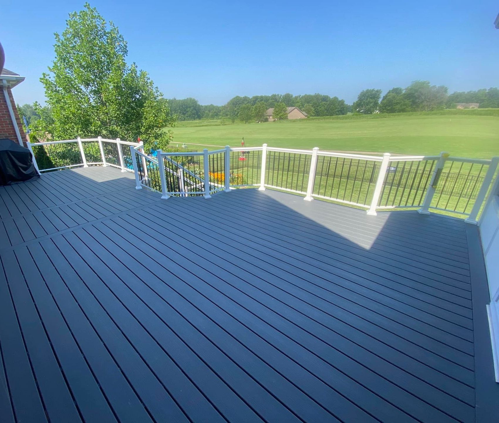Gray composite deck with white and black railings, overlooking a golf course.