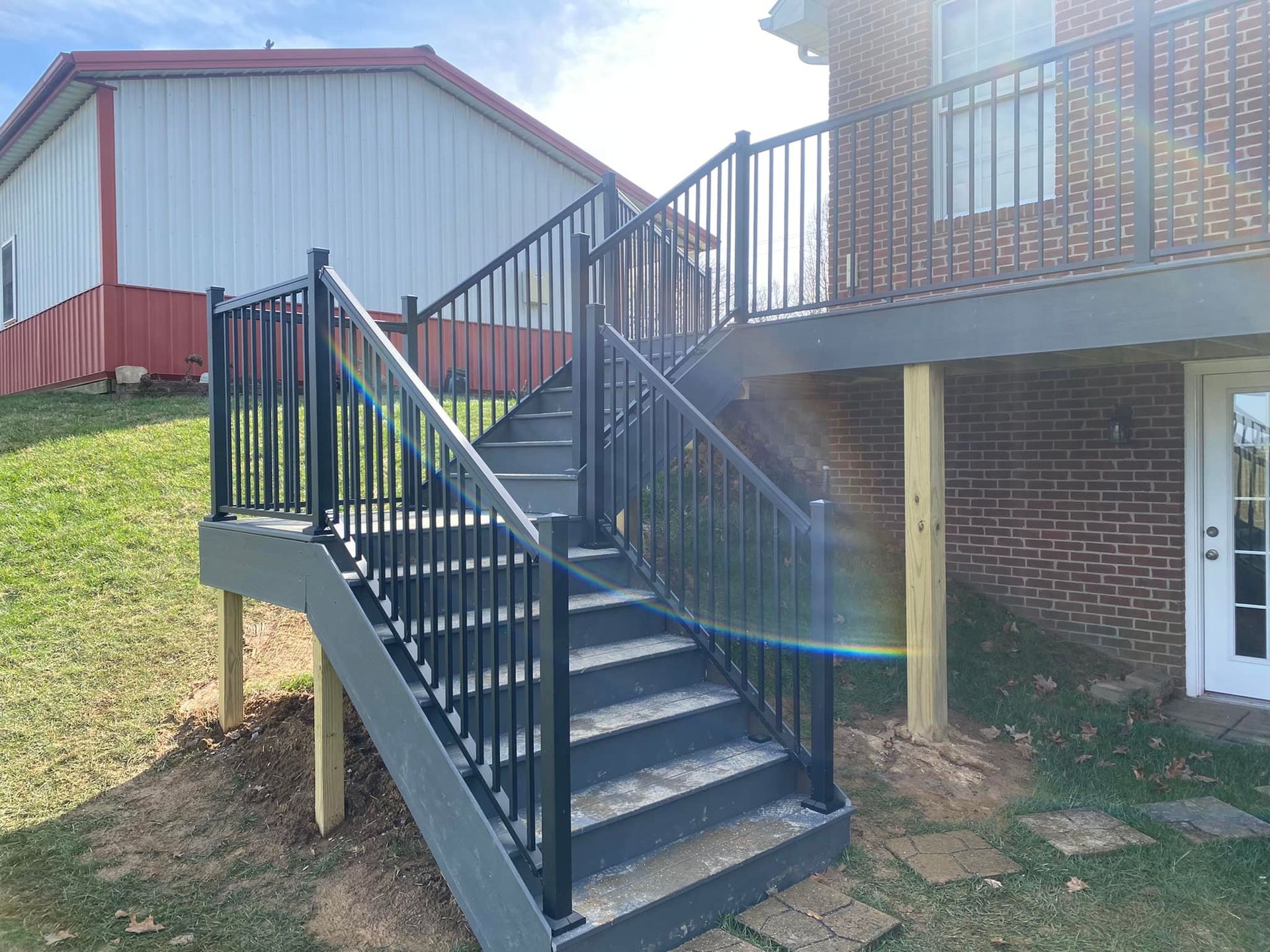 A deck with stairs leading up to it and a brick building in the background.