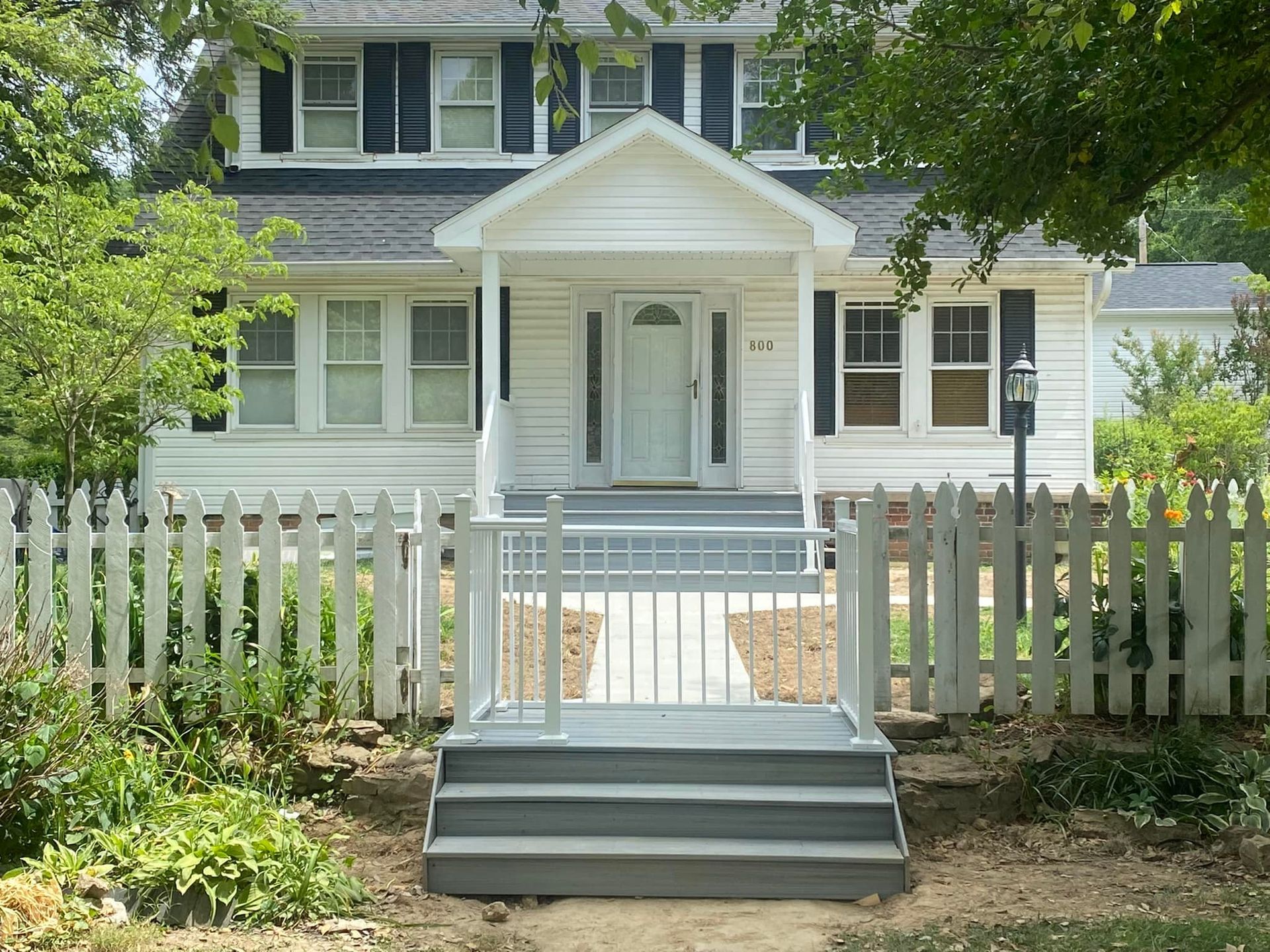 A white house with black shutters and a white picket fence