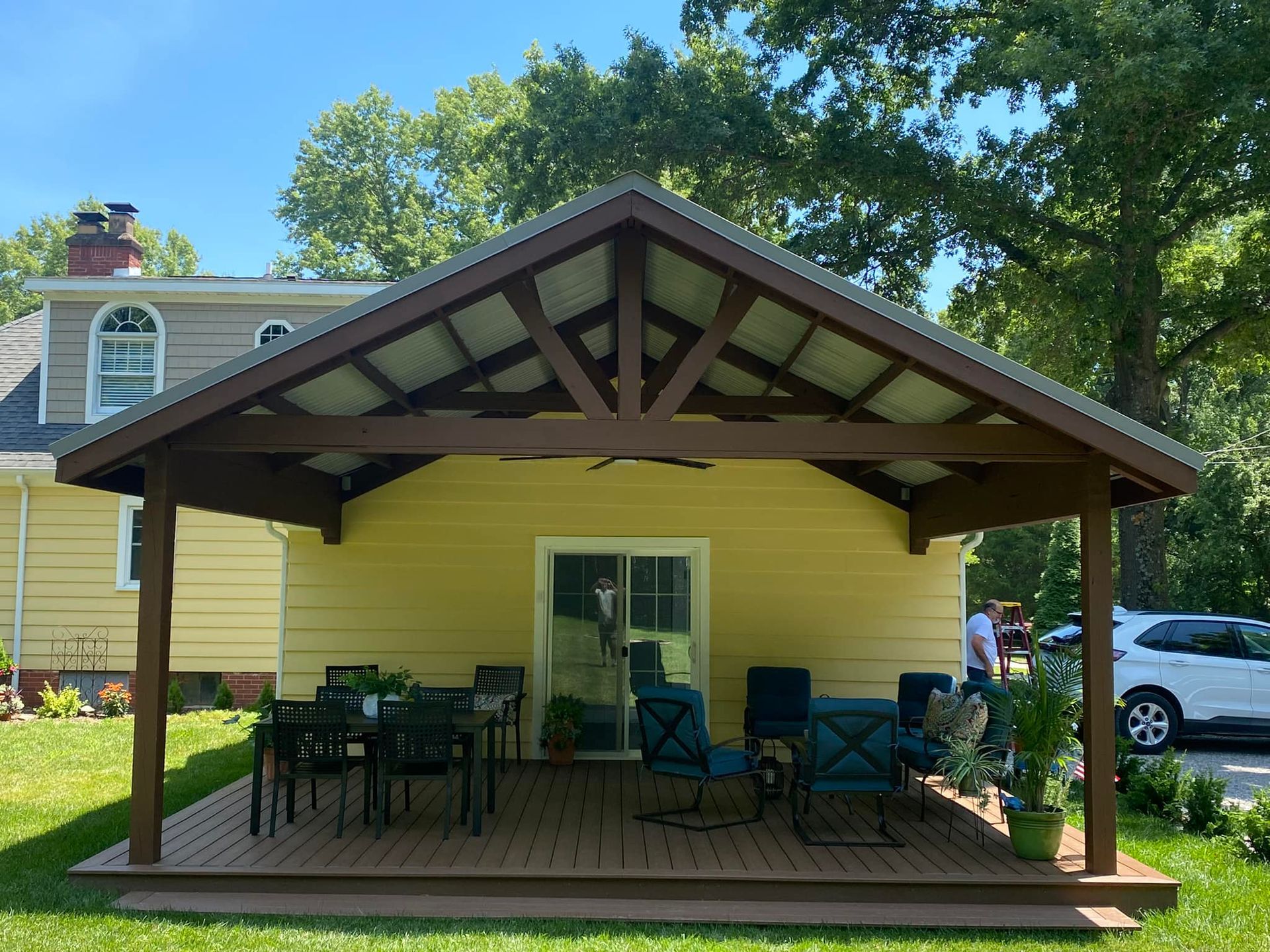 A yellow house with a wooden porch with a table and chairs underneath it