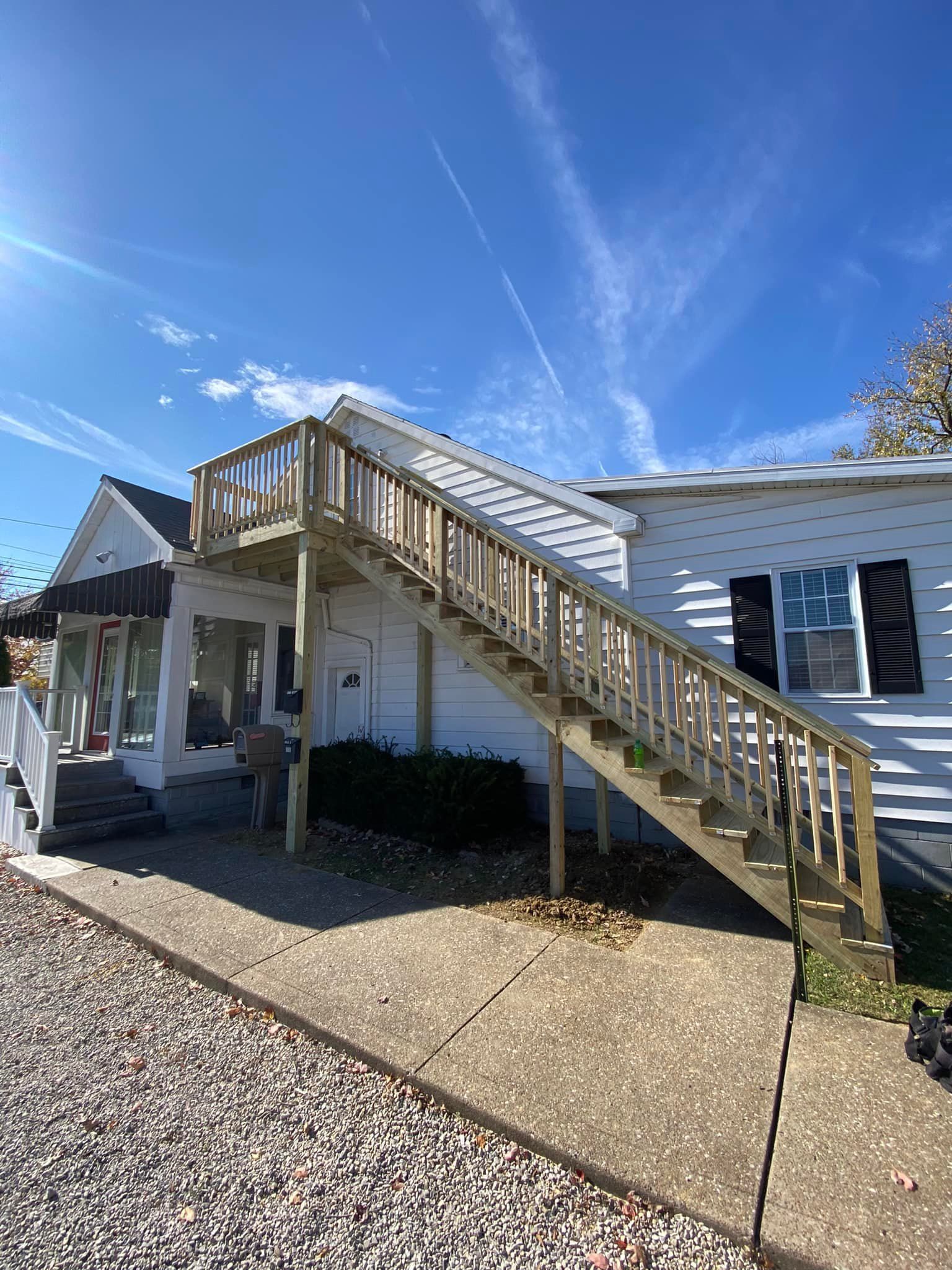 A white house with a wooden deck and stairs leading up to it.