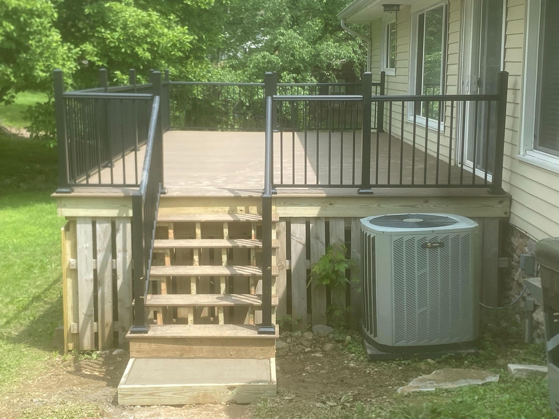 A deck with stairs and a air conditioner in the backyard of a house.
