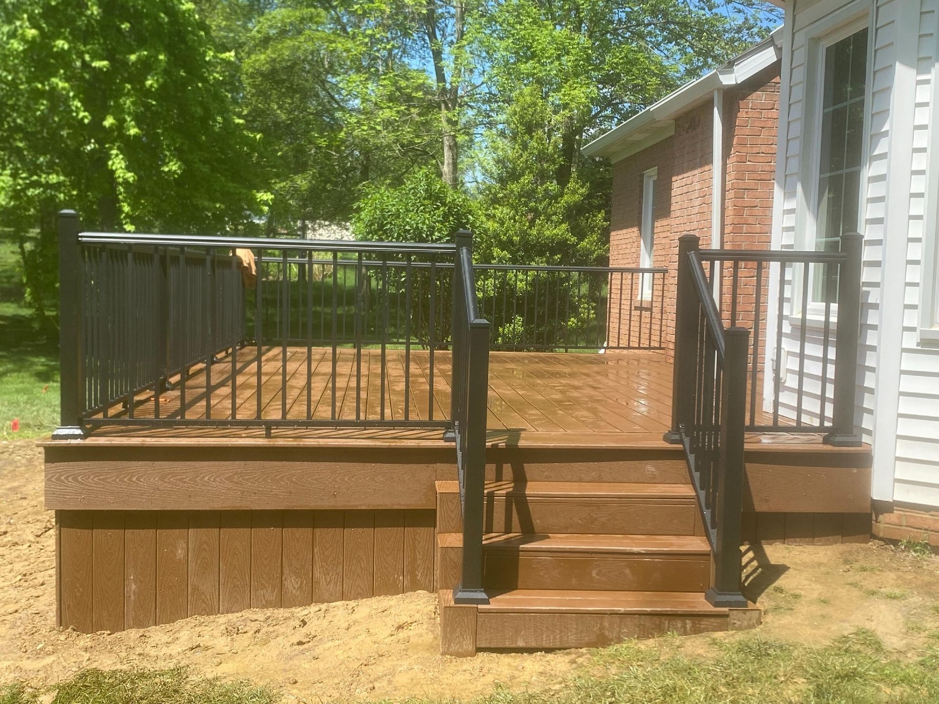 A wooden deck with stairs and a black railing is in front of a house.