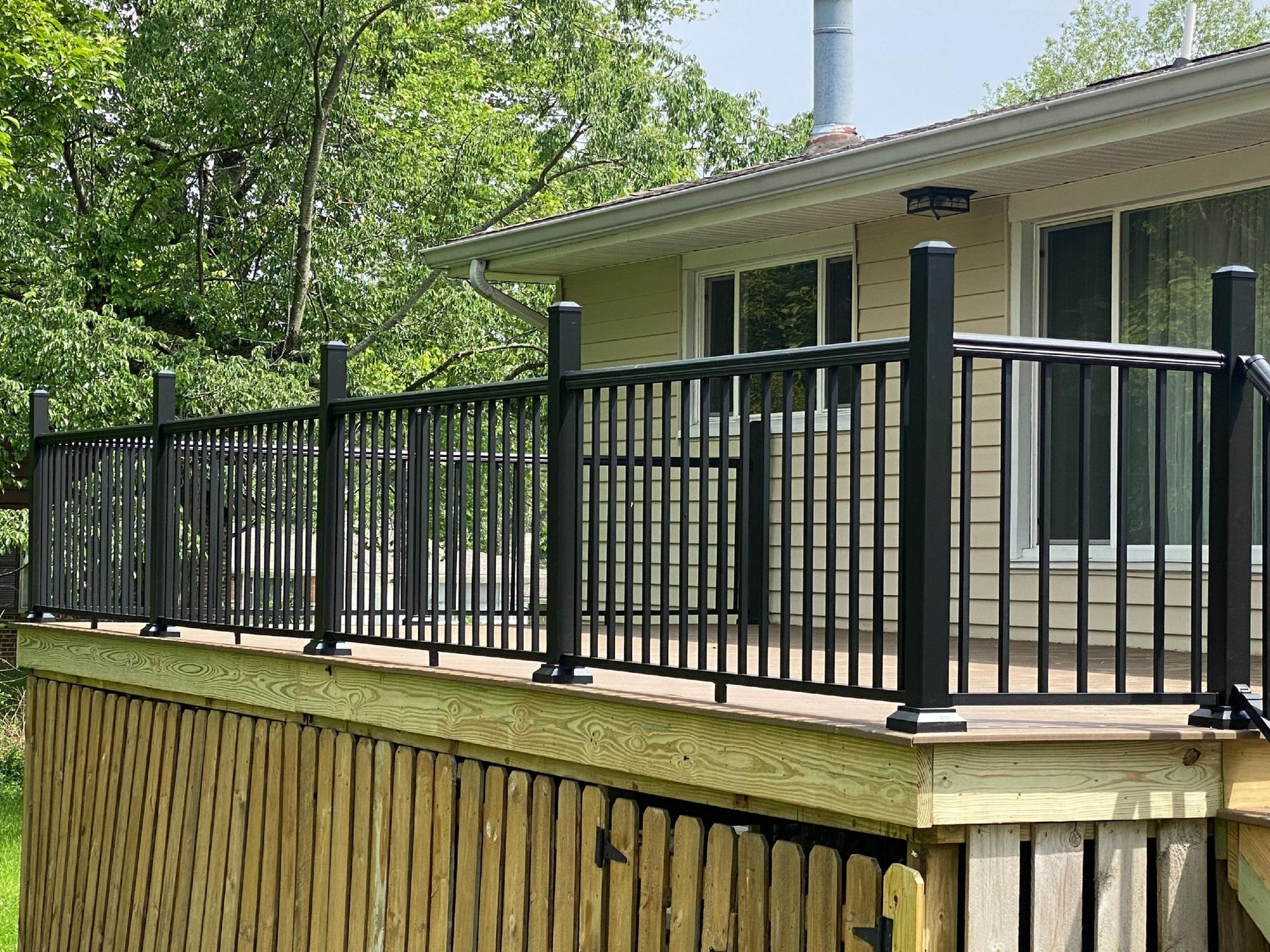 A deck with a black railing and a wooden fence in front of a house.